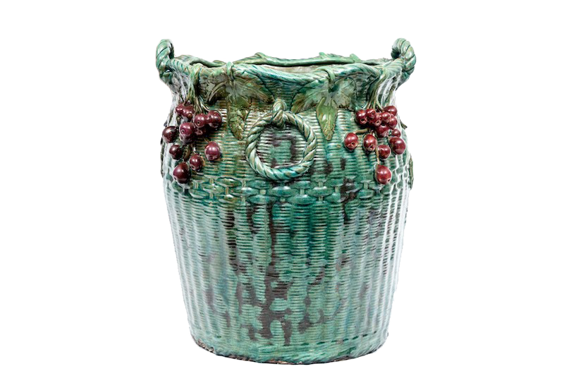A tall ceramic basket with cherries and leaves in mottled green and brown glaze